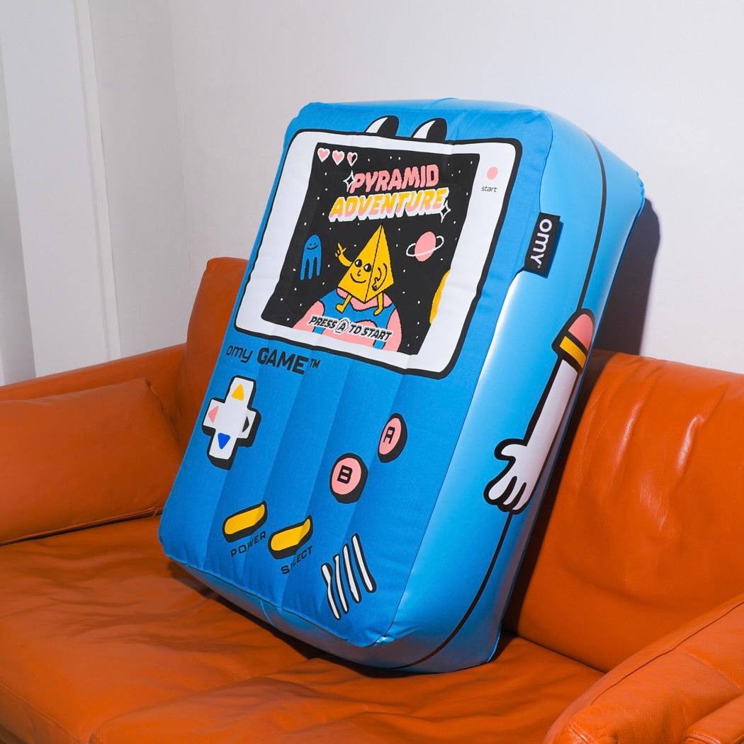 Blue game console-shaped pillow OMY on an orange couch