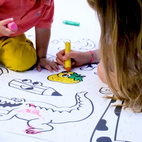 Two children drawing on a large sheet of paper with colorful markers.