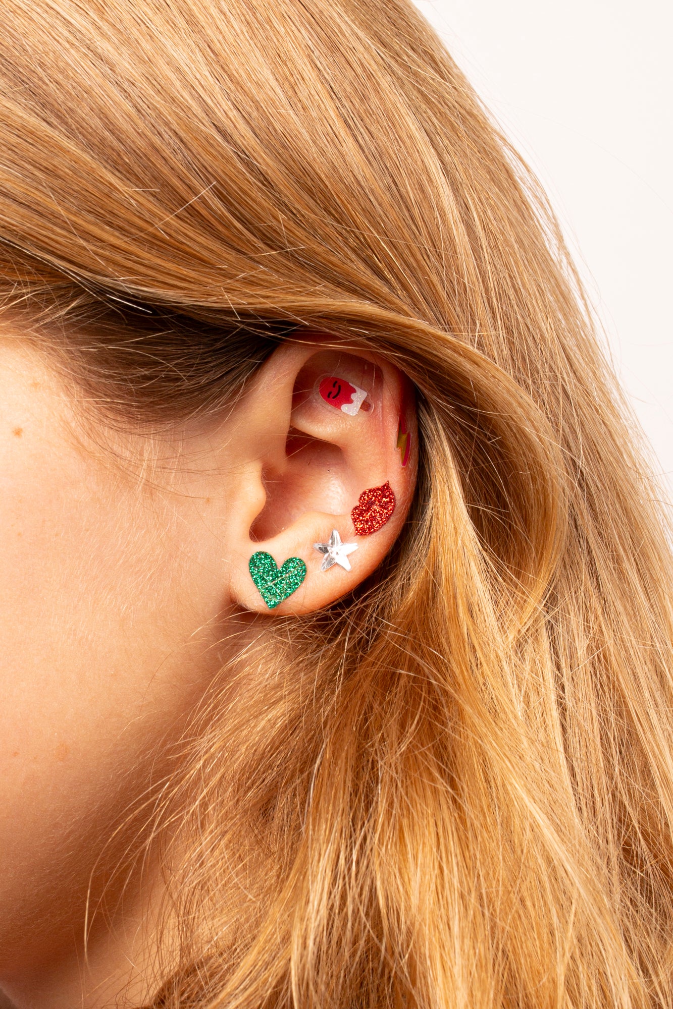 Close-up of an ear wearing colorful heart-shaped earrings Kawai OMY with blonde hair.