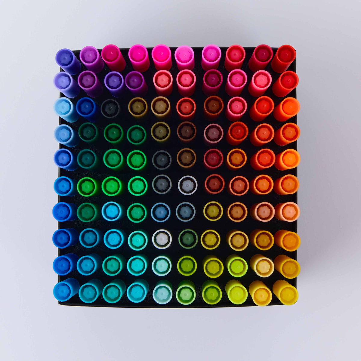 A top-down view of a 70-color marker OMY set arranged in a grid on a black square, showcasing a vibrant rainbow gradient of colors against a light gray background.