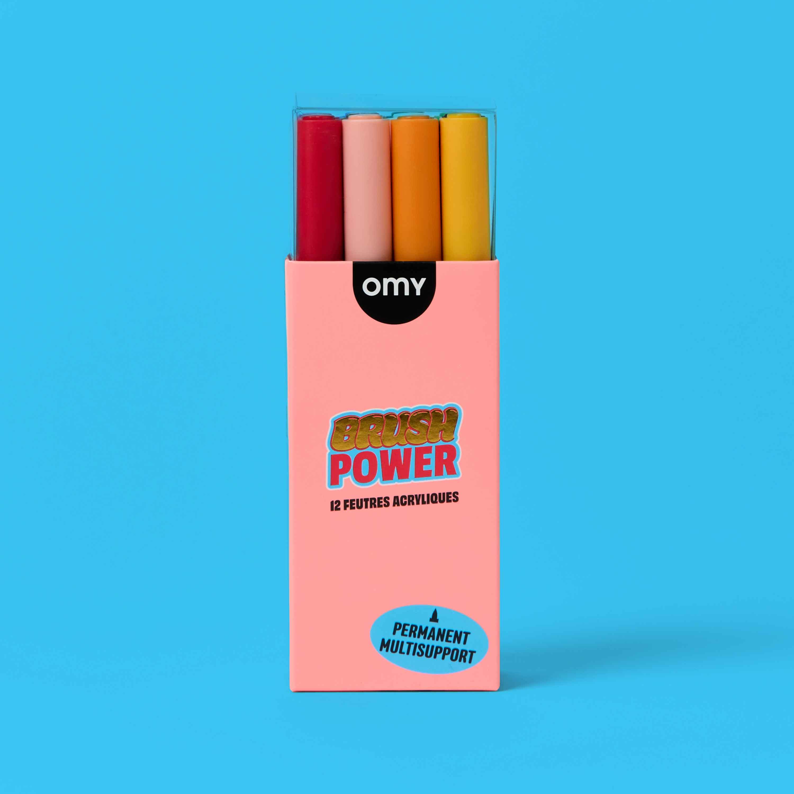 OMY Brush Power 12 acrylic markers front packaging – pink closed box with colorful marker caps, permanent multi-surface brush tip pens for art on blue background