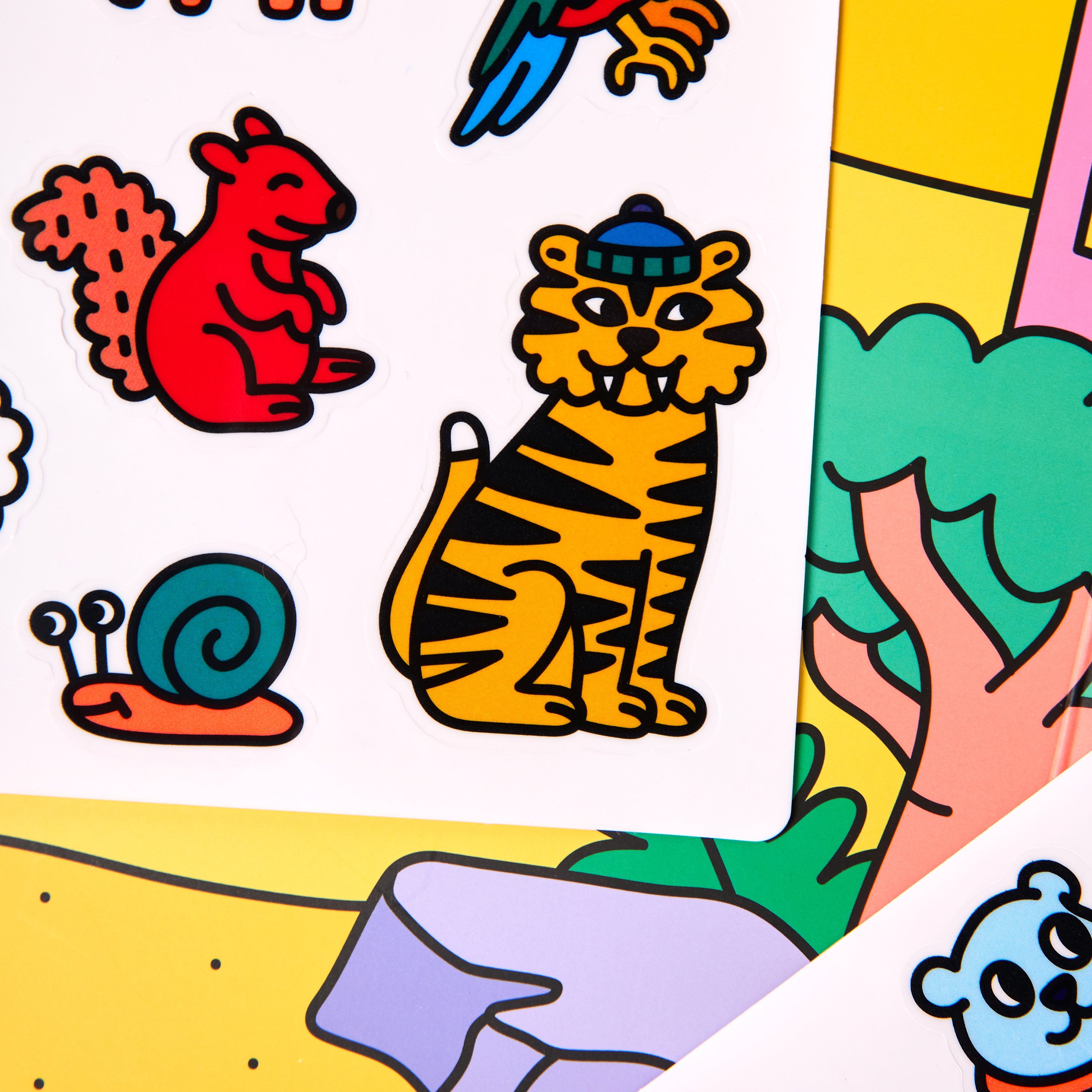 Close-up of Montessori animal sticker sheet featuring red squirrel, blue snail, and tiger stickers against colorful illustrated background.