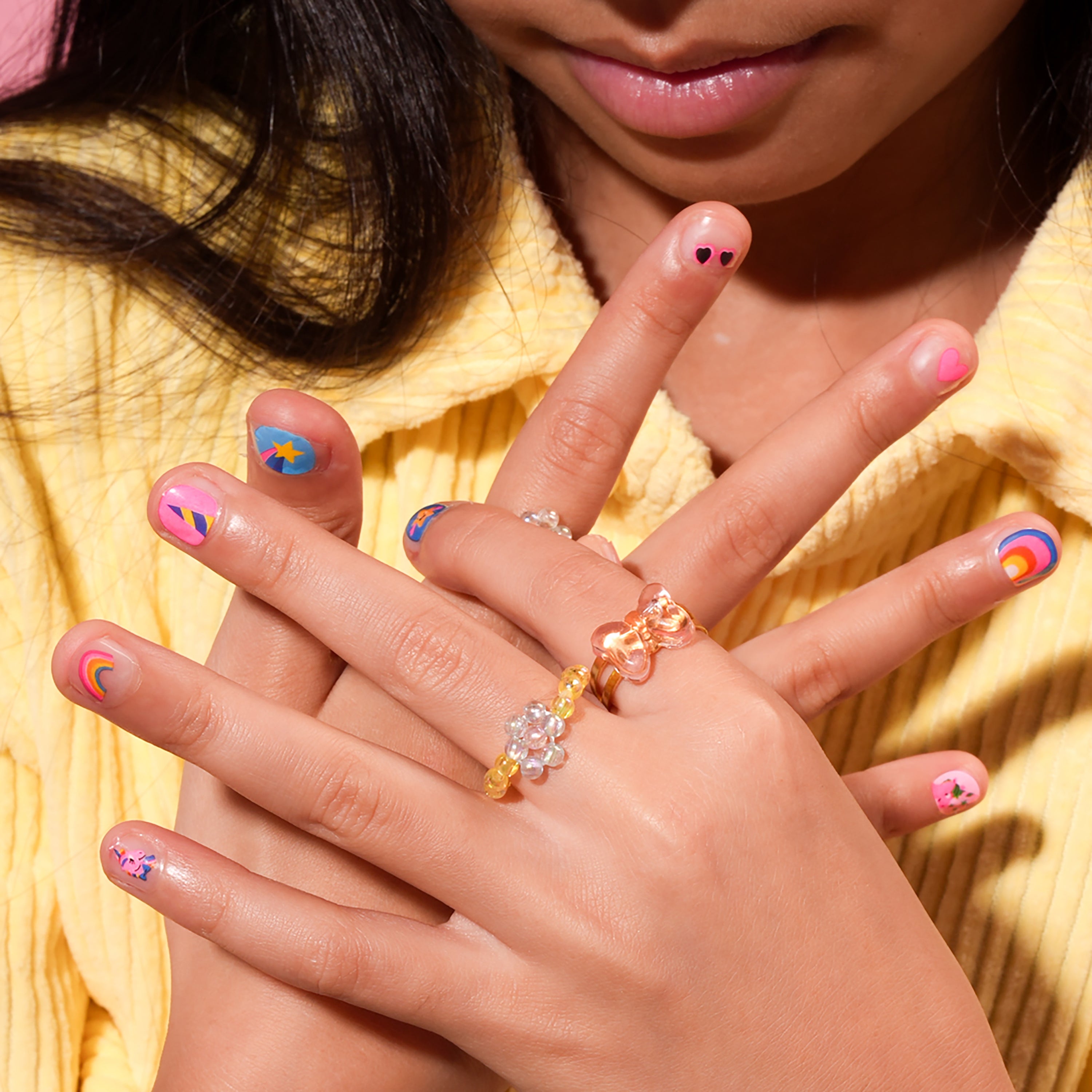 Close-up of a child's hands decorated with OMY unicorn nail stickers featuring rainbows, hearts, stars and other fun, colorful designs.