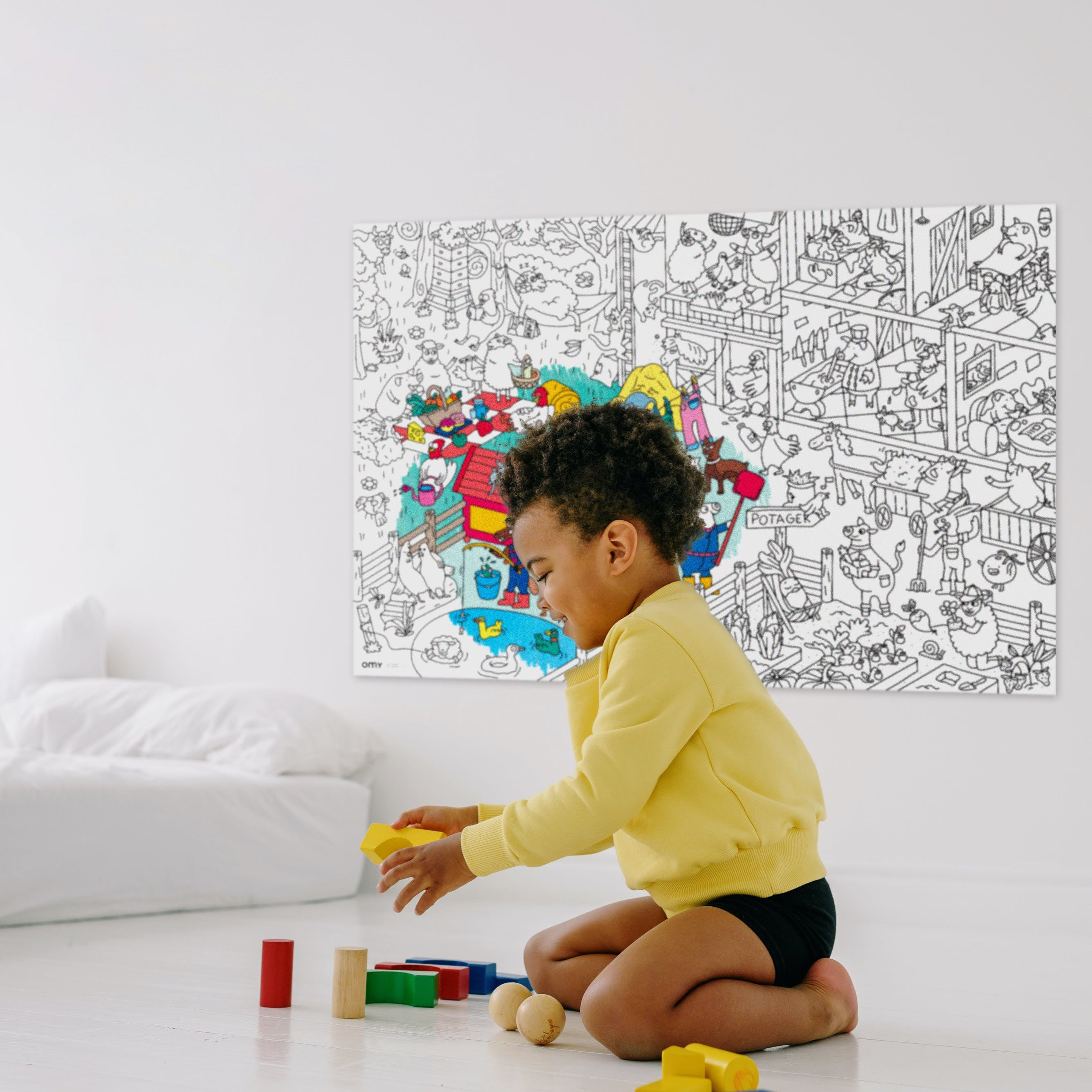 Child playing with blocks in front of a large coloring book OMY on a wall