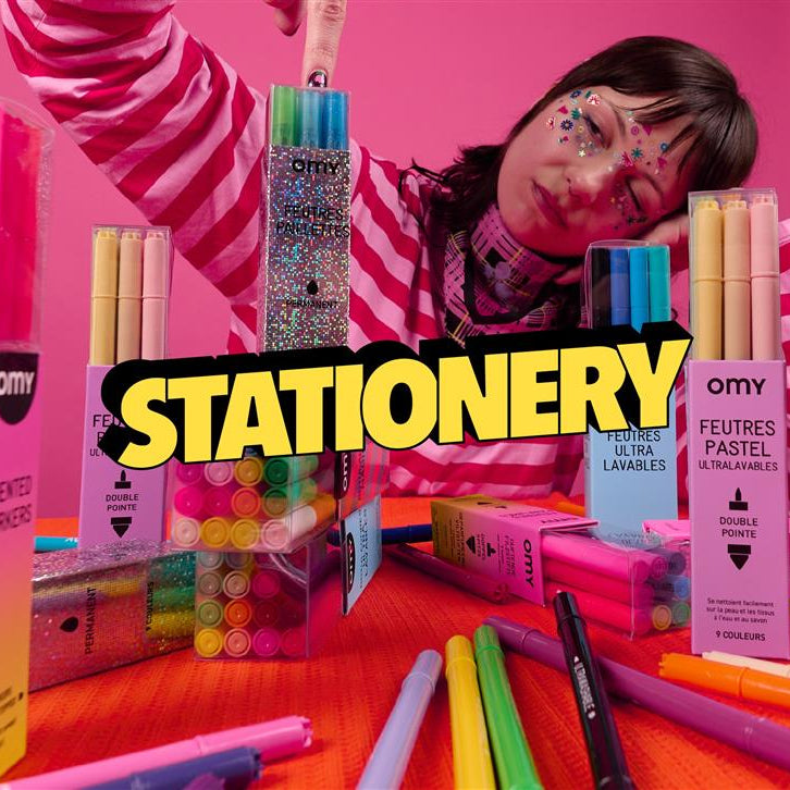 Person surrounded by colorful stationery items OMY on a pink background