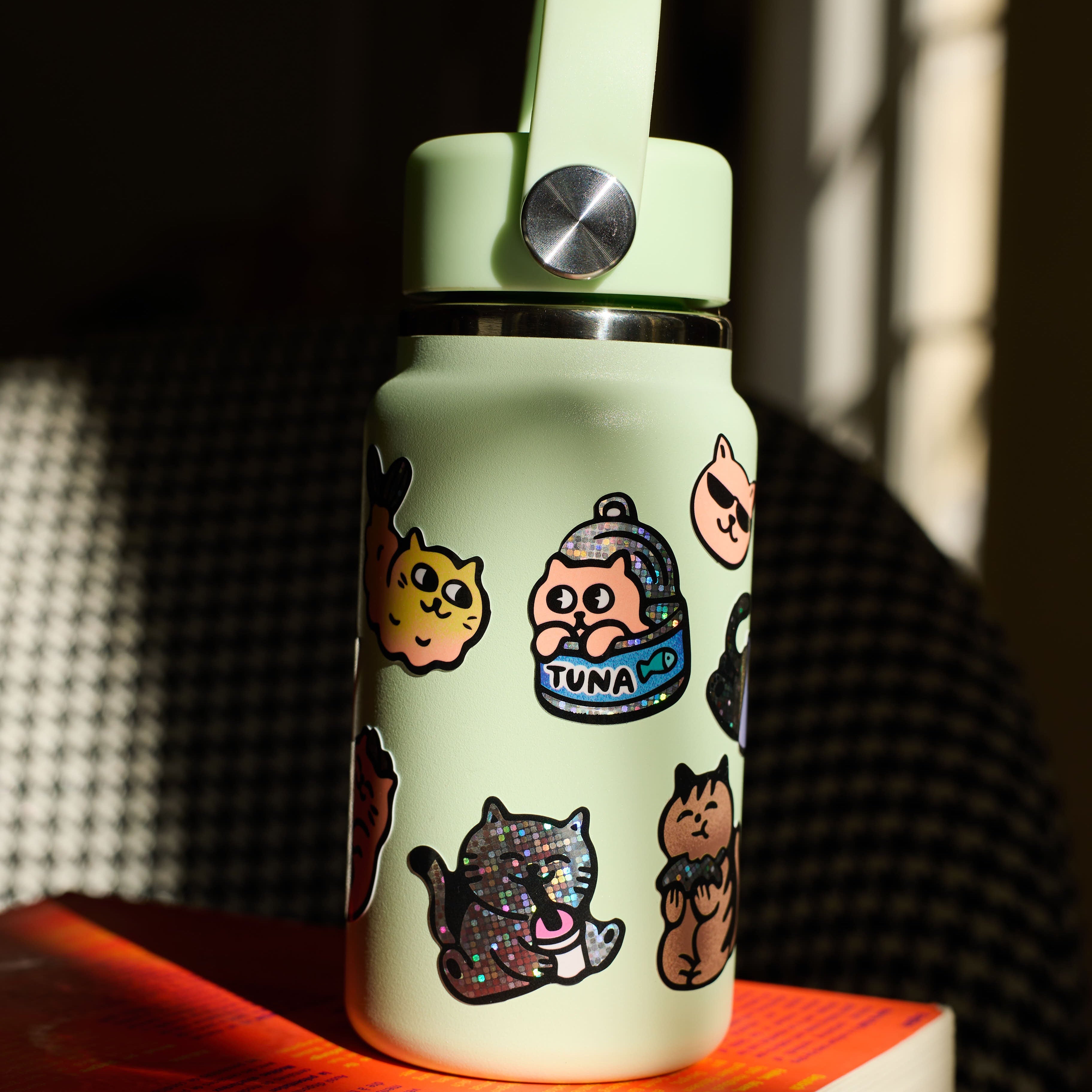 Light green water bottle with stickers big kitty OMY on a wooden surface