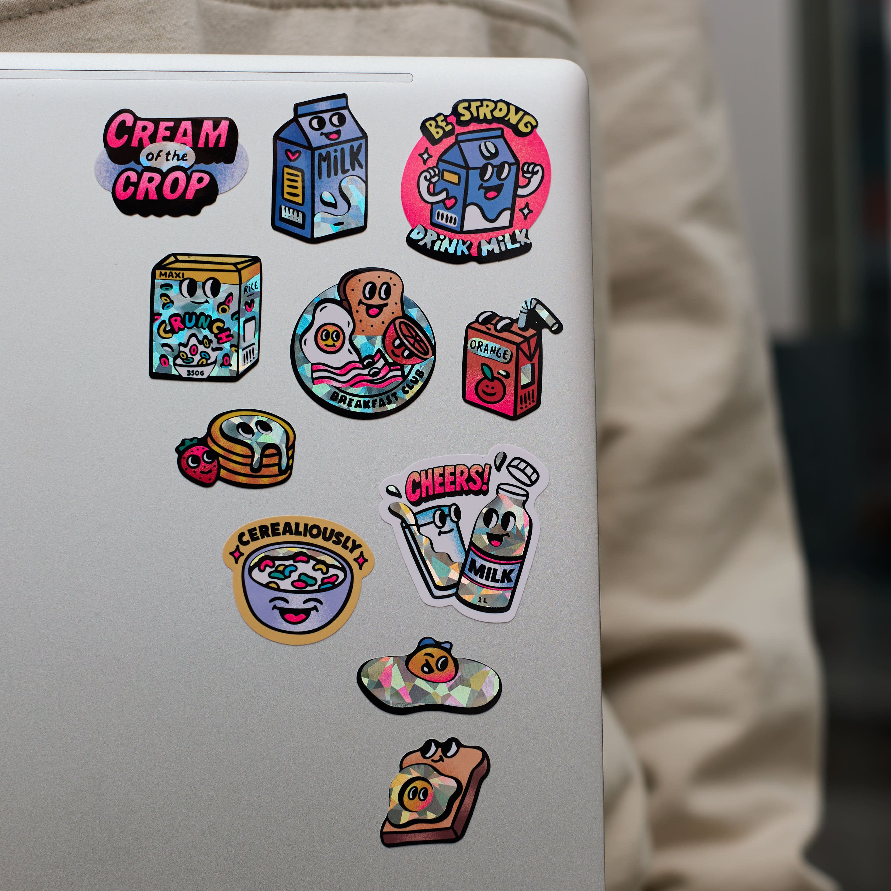 Sticker collection big milk OMY on a white surface with a person wearing a beige jacket in the background.