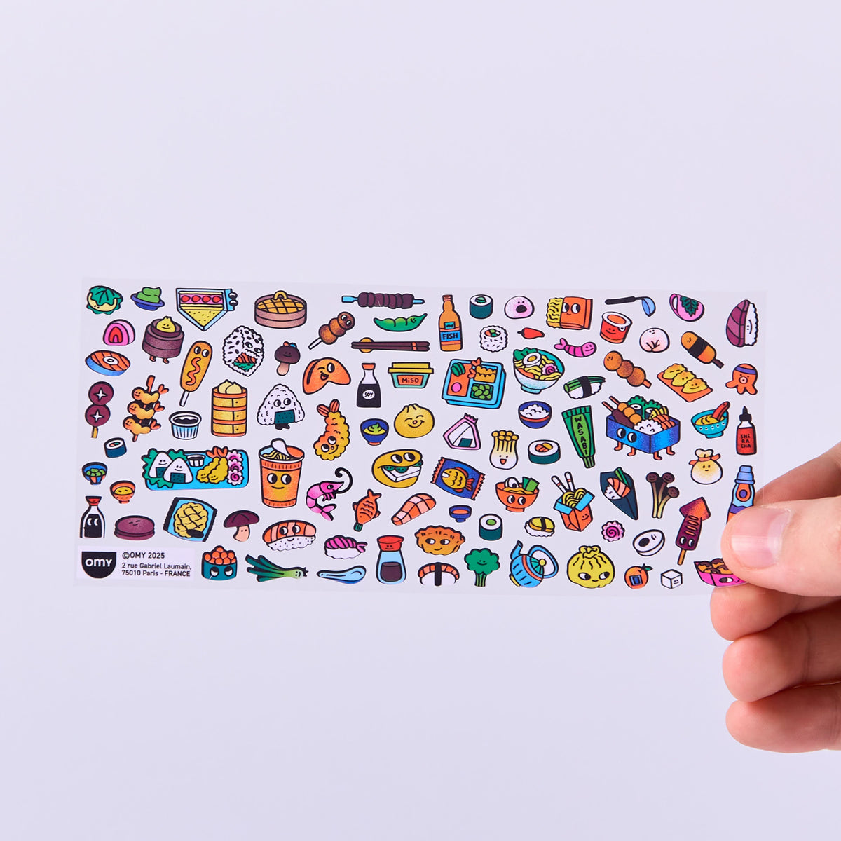 Sheet of colorful food-themed stickers OMY held by a hand on a light purple background
