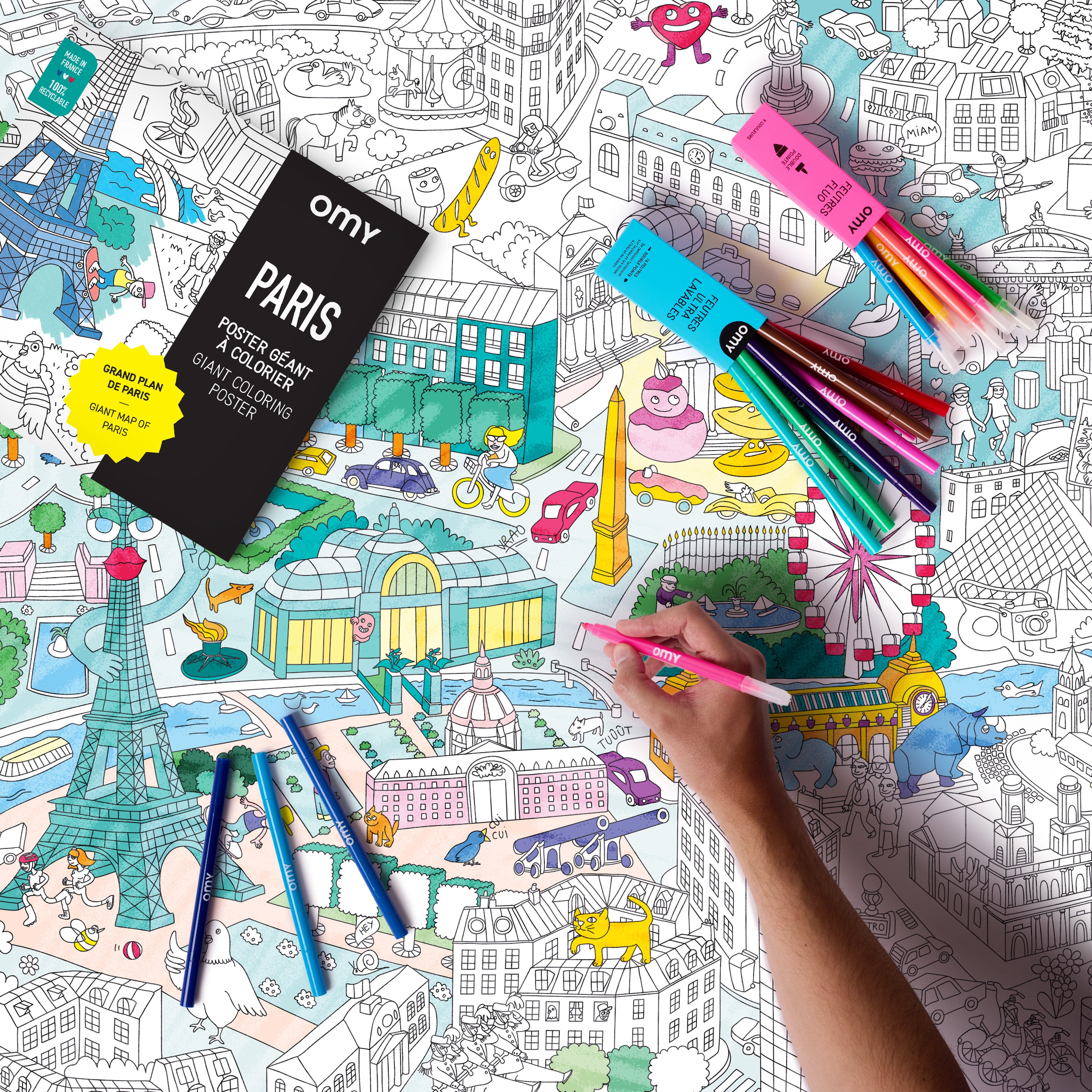  Child coloring OMY Paris giant poster with vibrant markers featuring Eiffel Tower, Arc de Triomphe and iconic landmarks of the city.