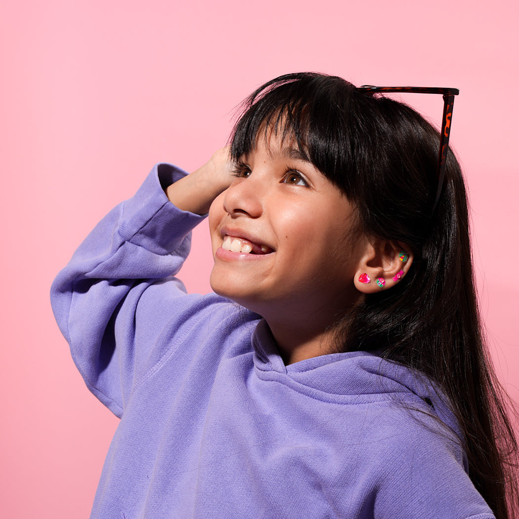 Young girl wearing a purple hoodie with OMY LILY earrings against a pink background