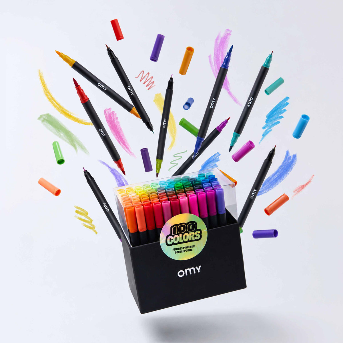 A set of 100 OMY dual-tip markers in a black box, shown with colorful paint swatches and marker caps flying out from the open box against a clean white background.