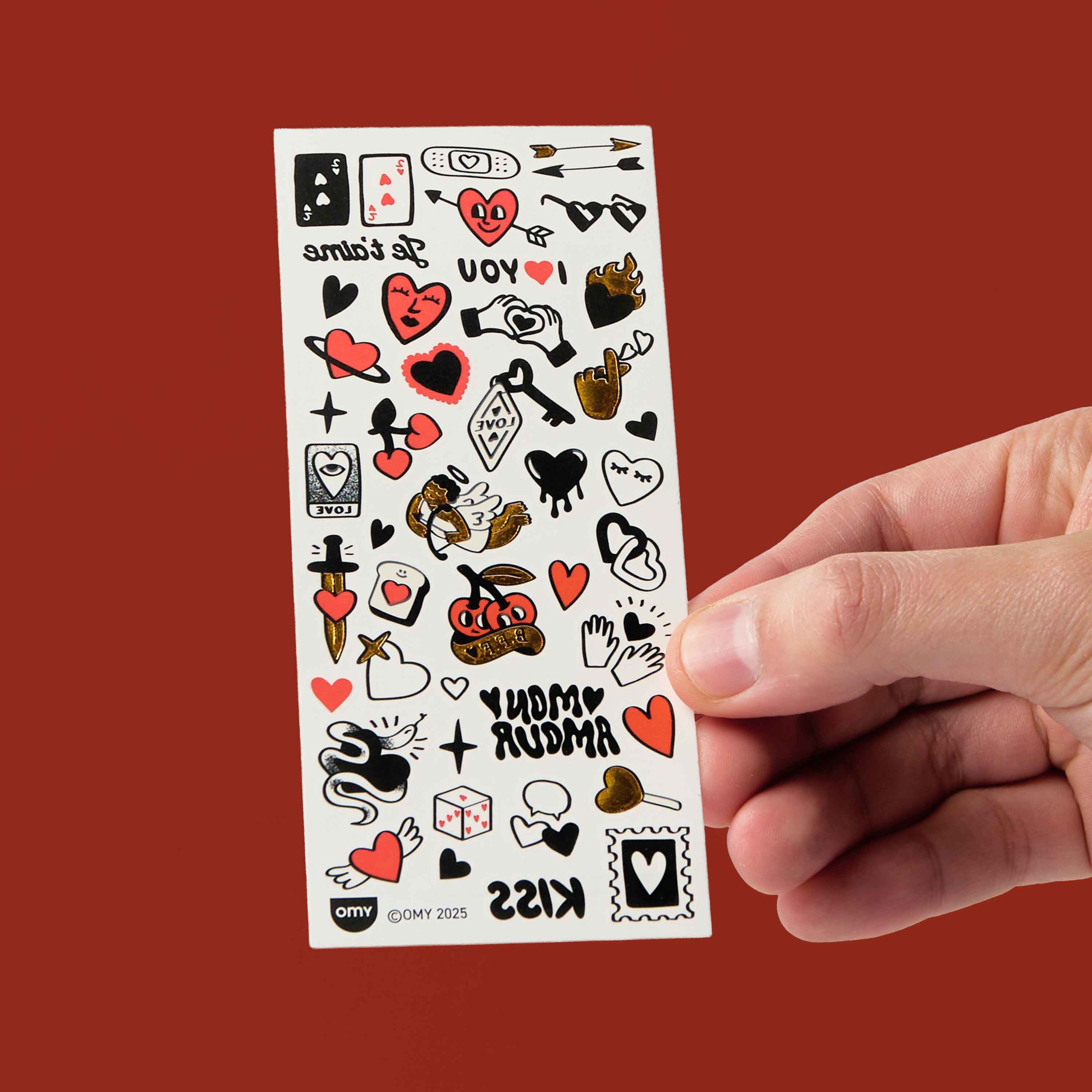 Sheet of flash tattoos OMY held by a hand against a red background