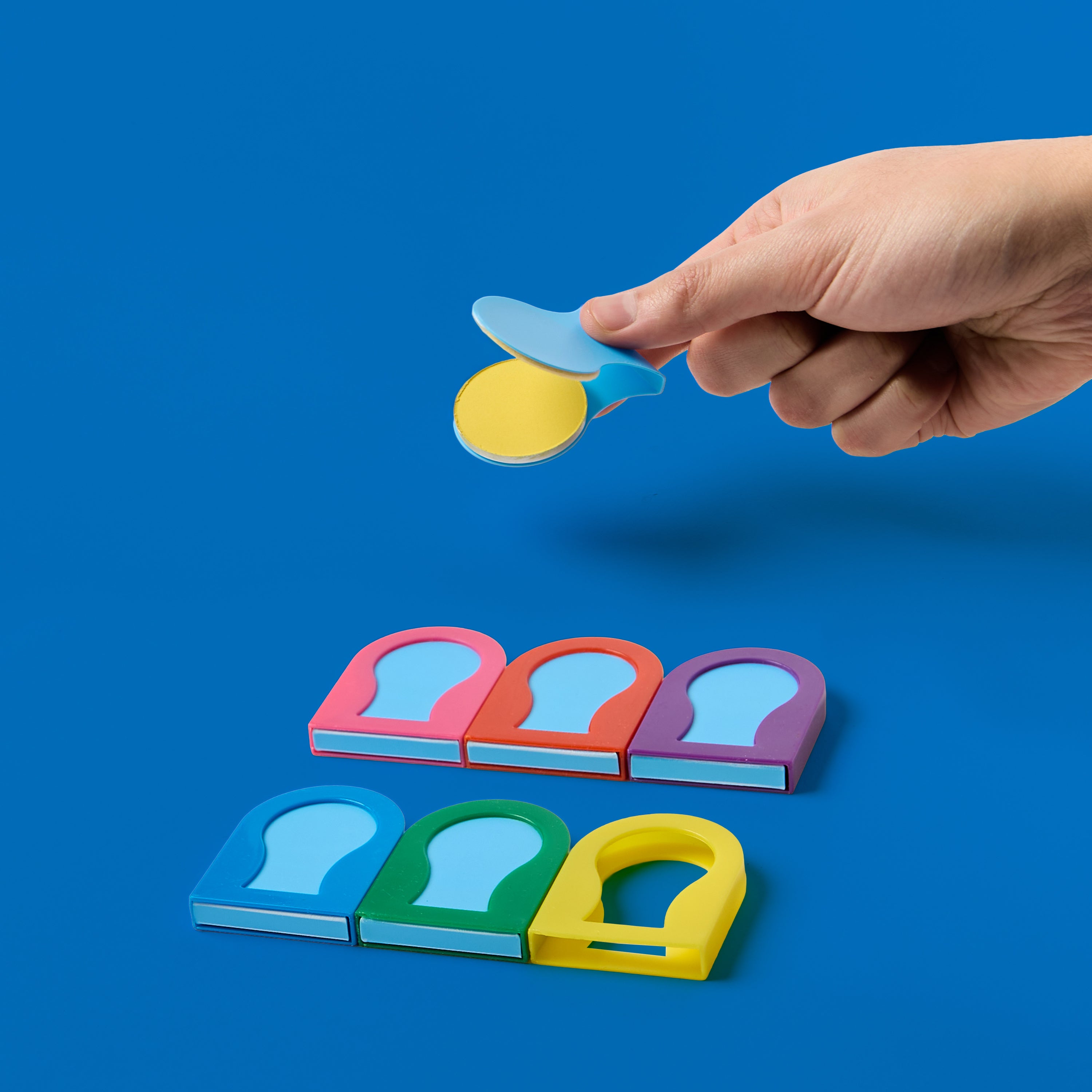 Hand holding an open OMY Hair Color Rainbow chalk pod with 6 colorful hair chalk applicators – pink, red, purple, blue, green and yellow on blue background