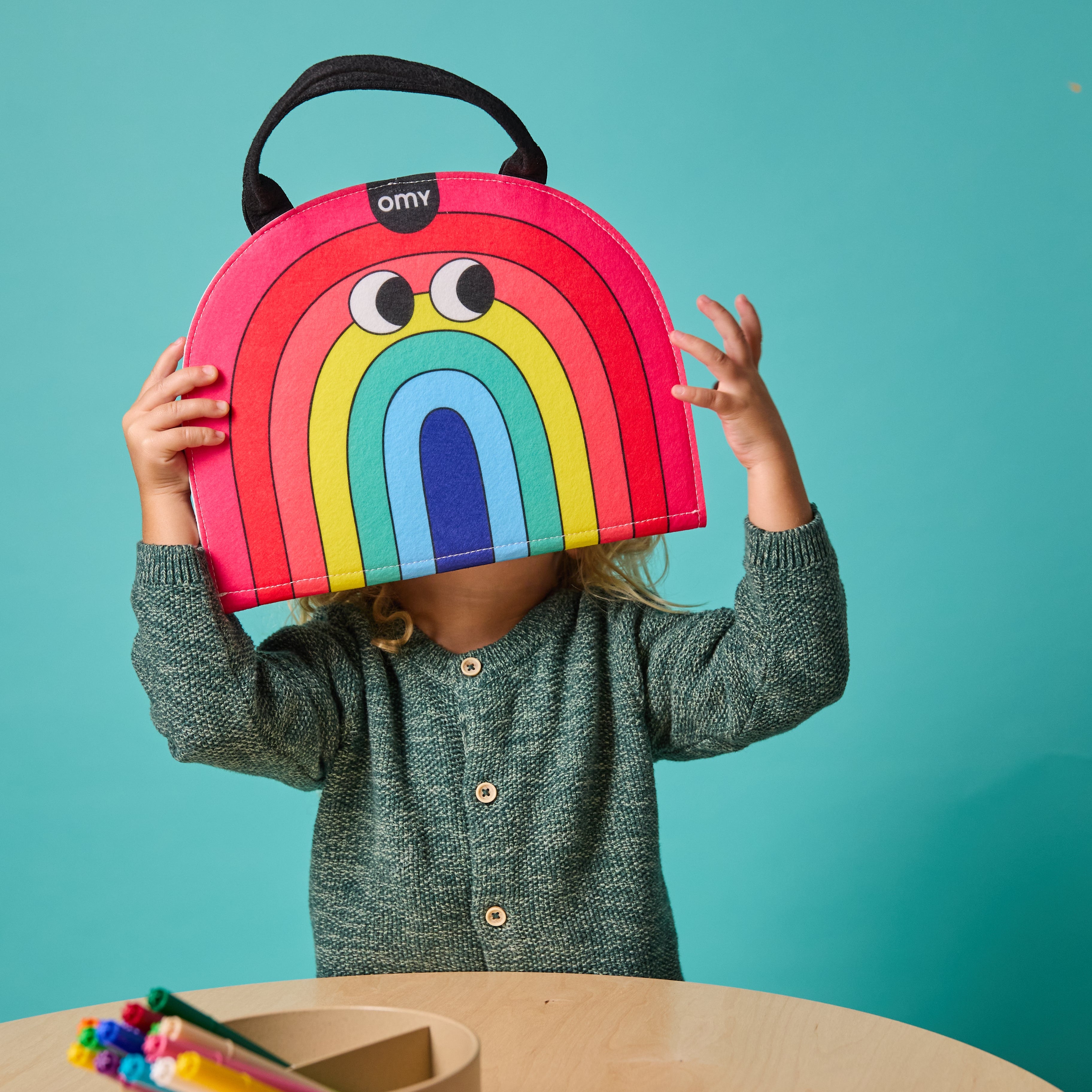 Toddler holding rainbow-shaped Montessori playkit — fun portable learning toy for shapes and colors.
