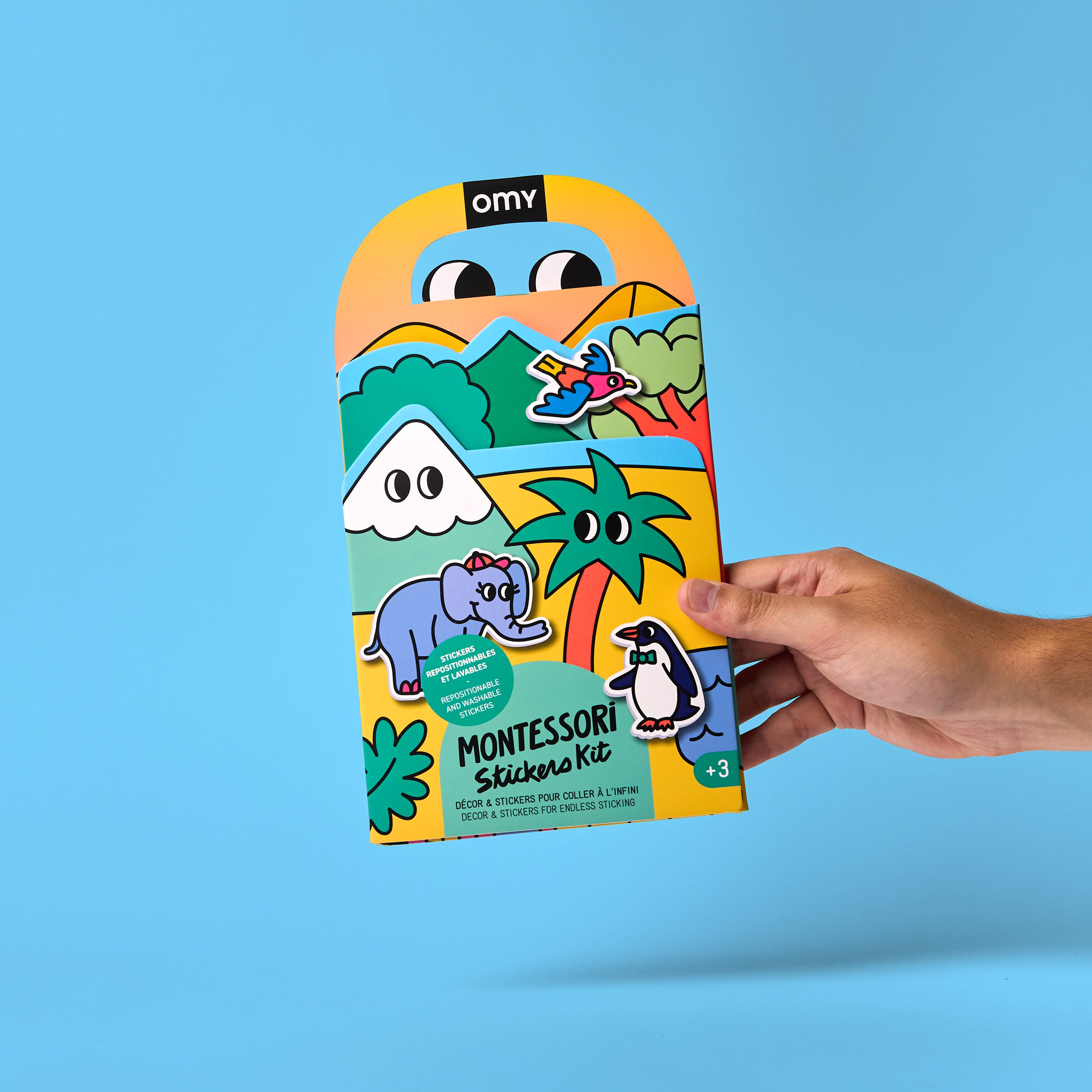 Hand holding Montessori sticker kit packaging with colorful animal illustrations on blue background.