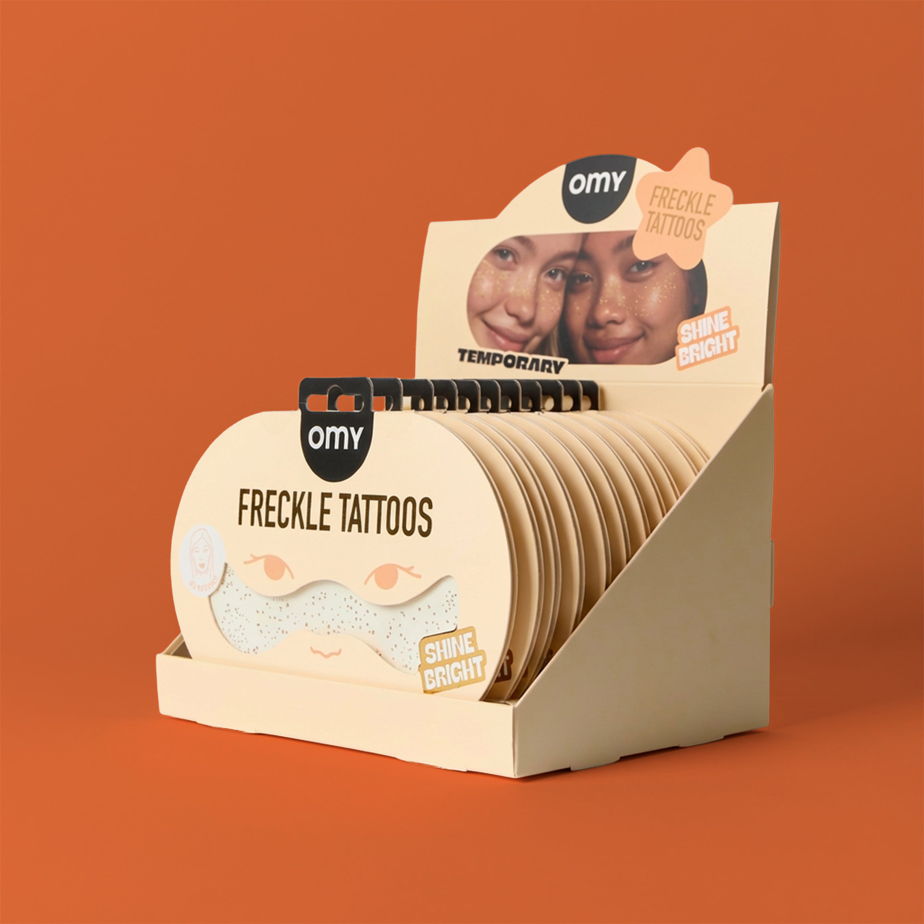 Display of OMY freckle tattoos with packaging on an orange background