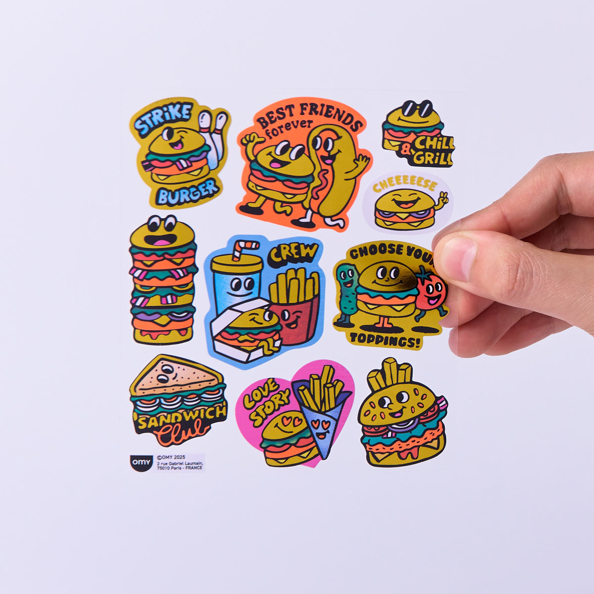 Colorful cartoon-style food and drink stickers OMY on a white background with a hand holding one sticker.