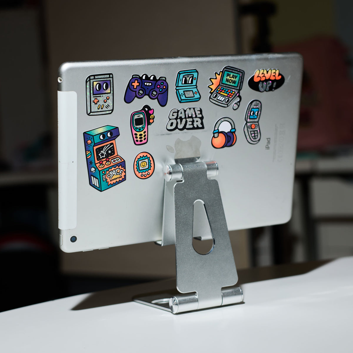Silver tablet stand with colorful big stickers game boy OMY on a blurred background