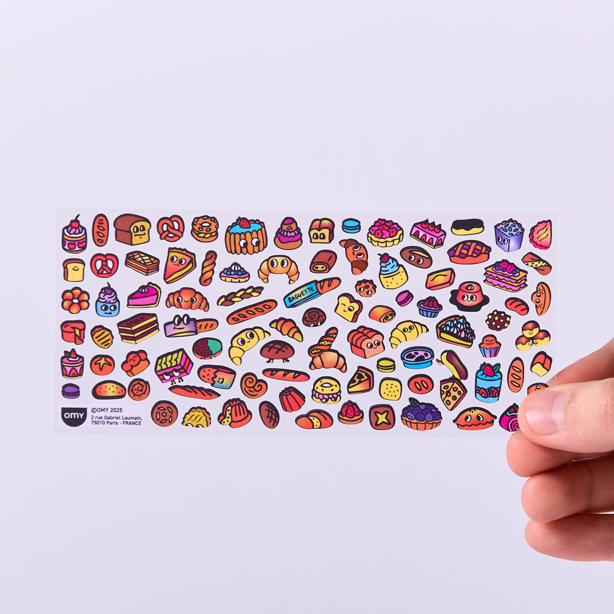Colorful food-themed stickers OMY held by a hand on a light purple background