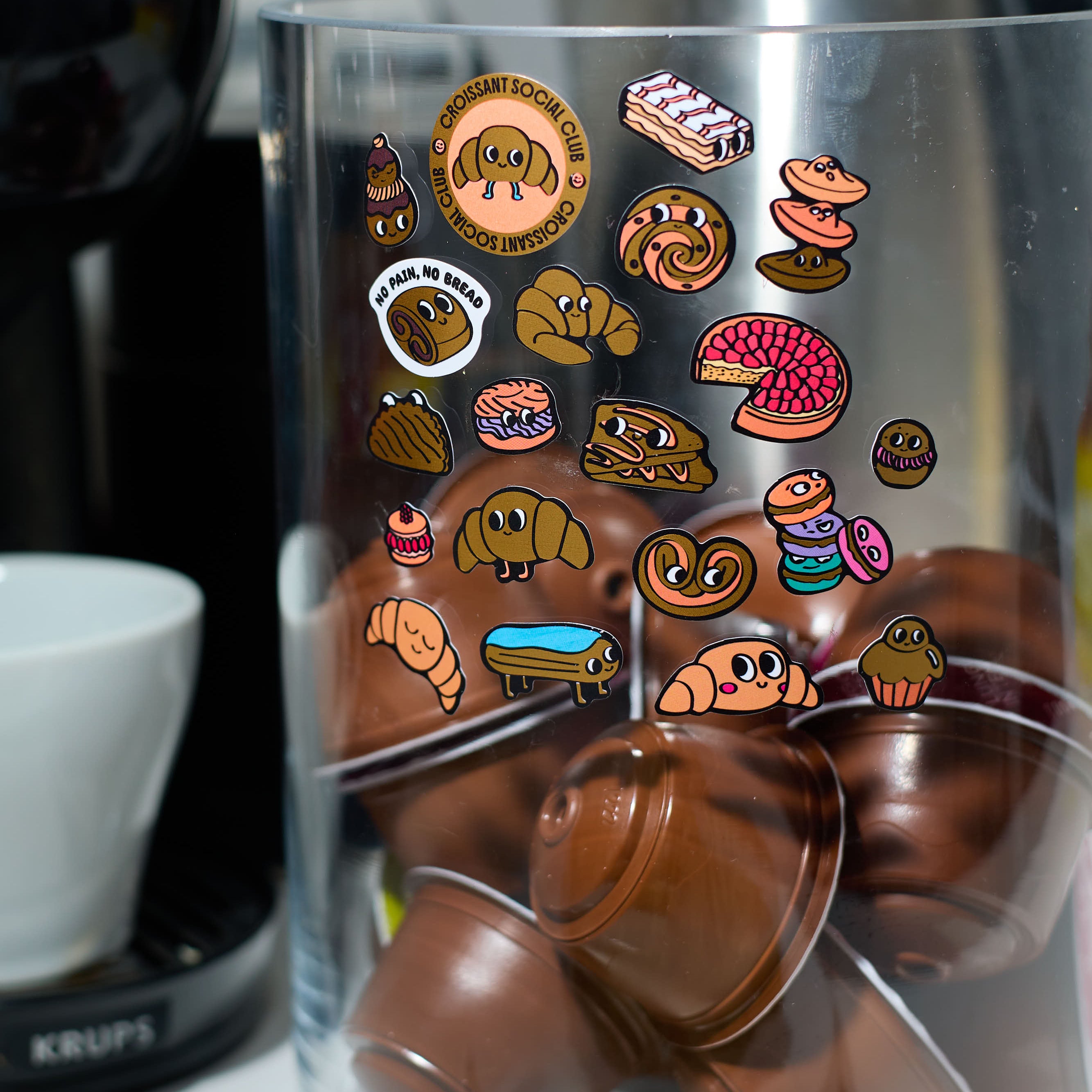 Glass container with chocolate capsules and colorful fabulous stickers on a kitchen counter.