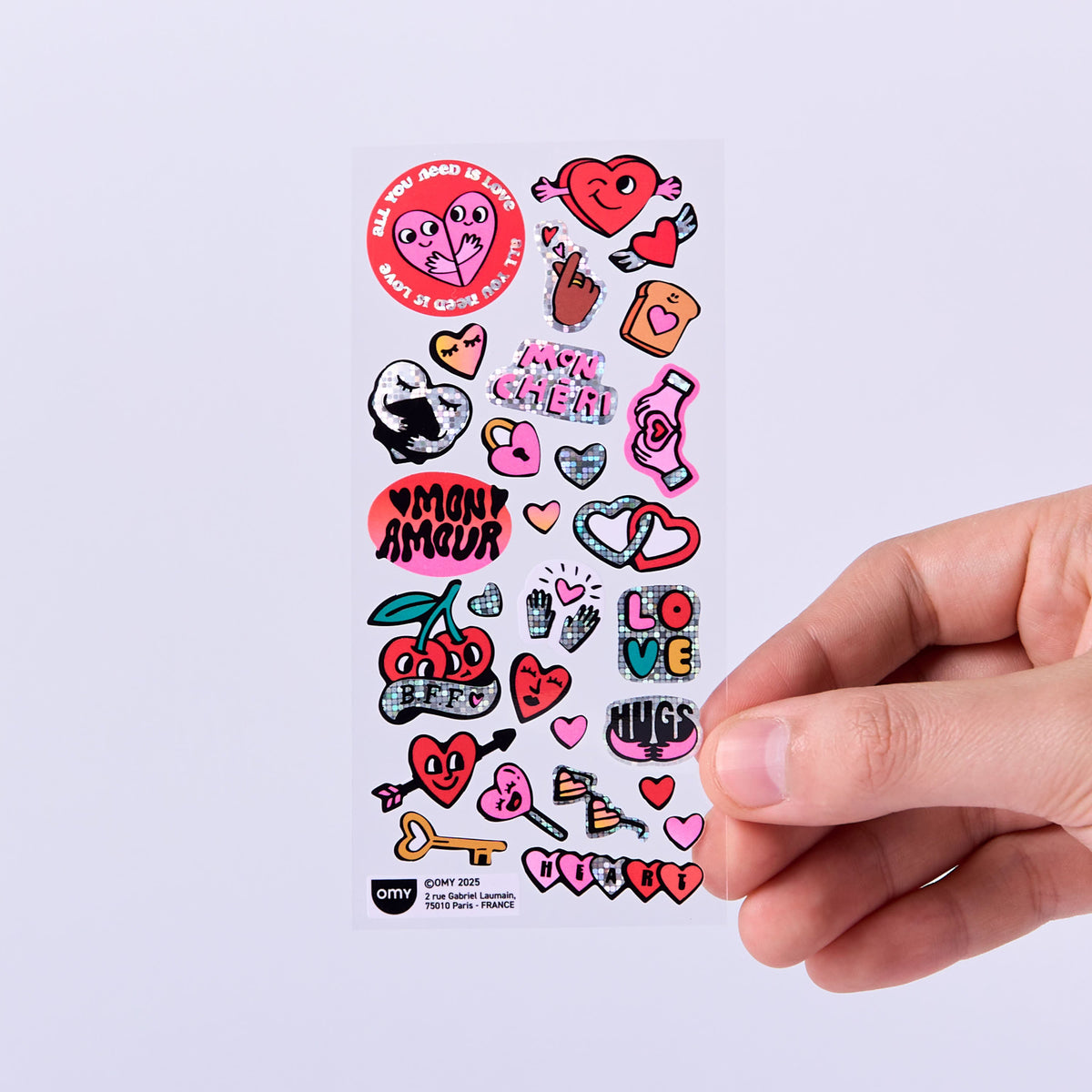 Sheet of colorful stickers iconic love OMY with various designs held by a hand on a light purple background