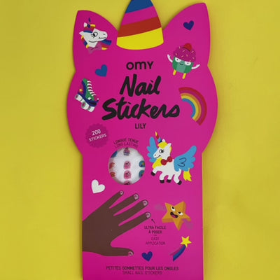 Close-up of child's hands applying colorful unicorn nail stickers from OMY on a yellow background.
